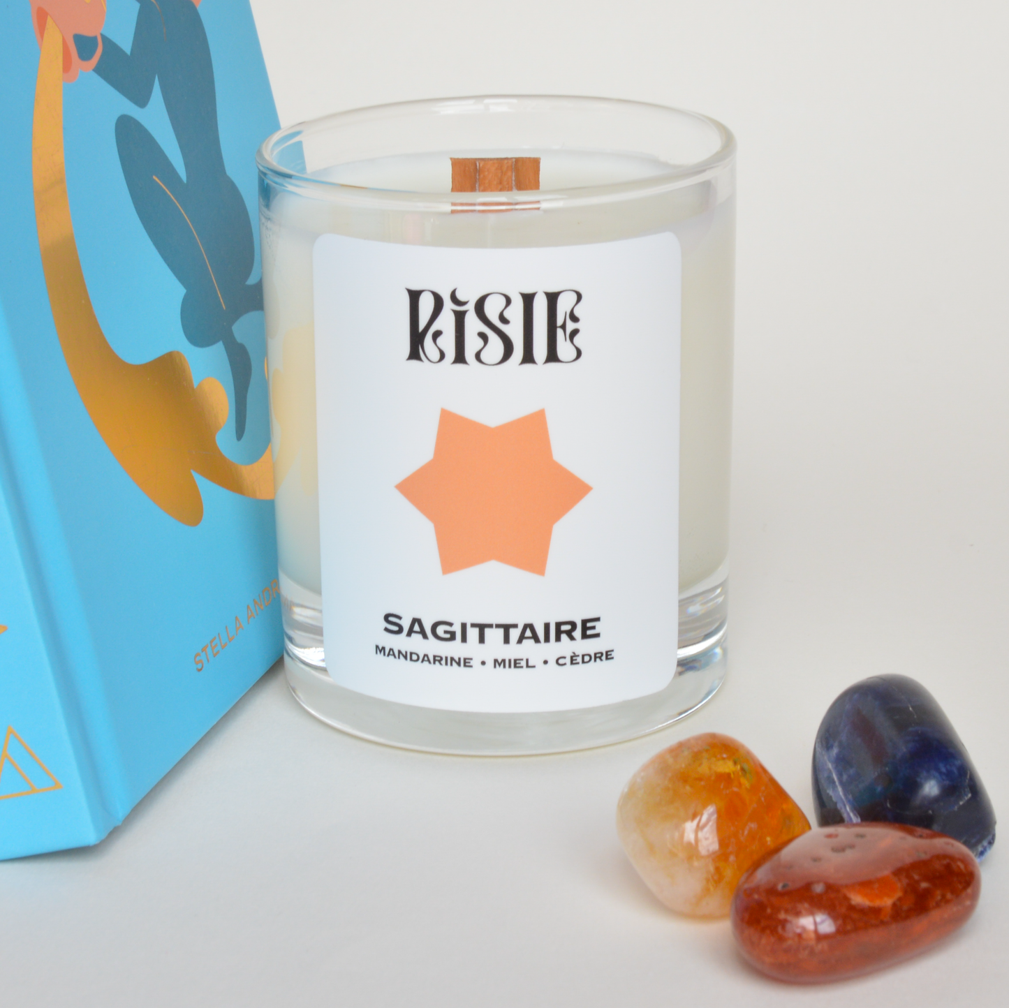 Photo de la bougie parfumée imaginée pour le signe astrologique du Sagittaire. On voit la bougie, des livres sur l'astrologie et des cristaux.