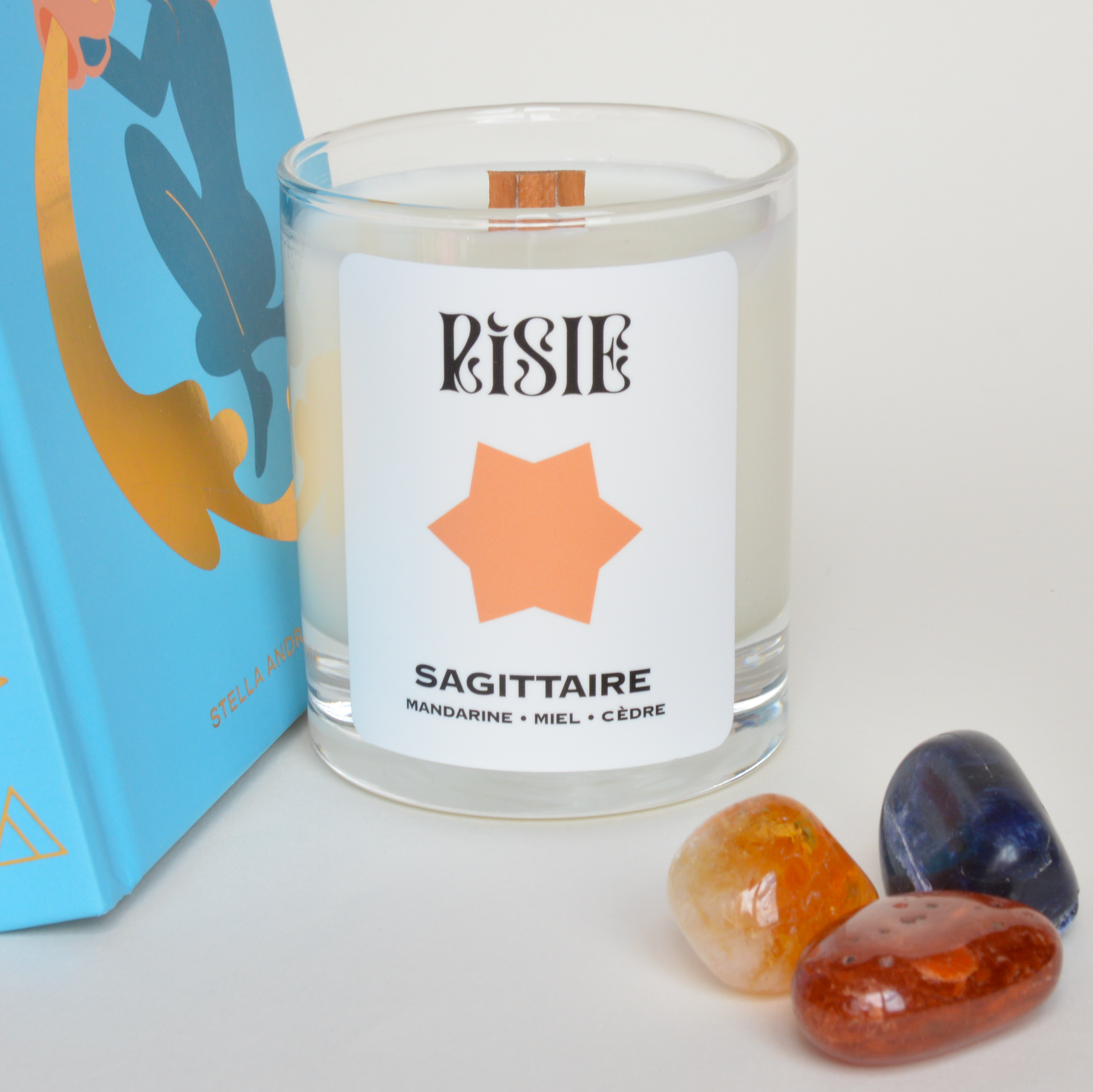 Photo de la bougie parfumée imaginée pour le signe astrologique du Sagittaire. On voit la bougie, des livres sur l'astrologie et des cristaux.