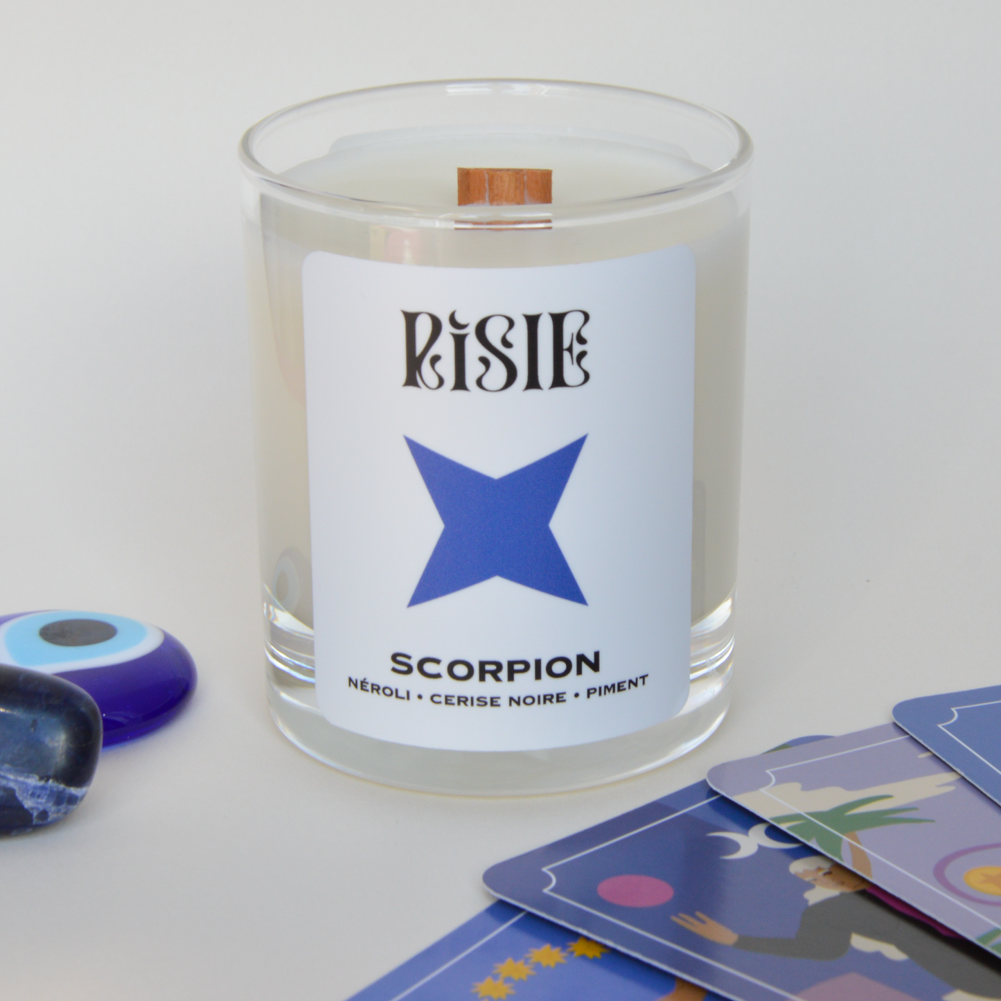 Photo de la bougie parfumée imaginée pour le signe astrologique du Scorpion. On voit la bougie, des cartes de tarot et des cristaux.